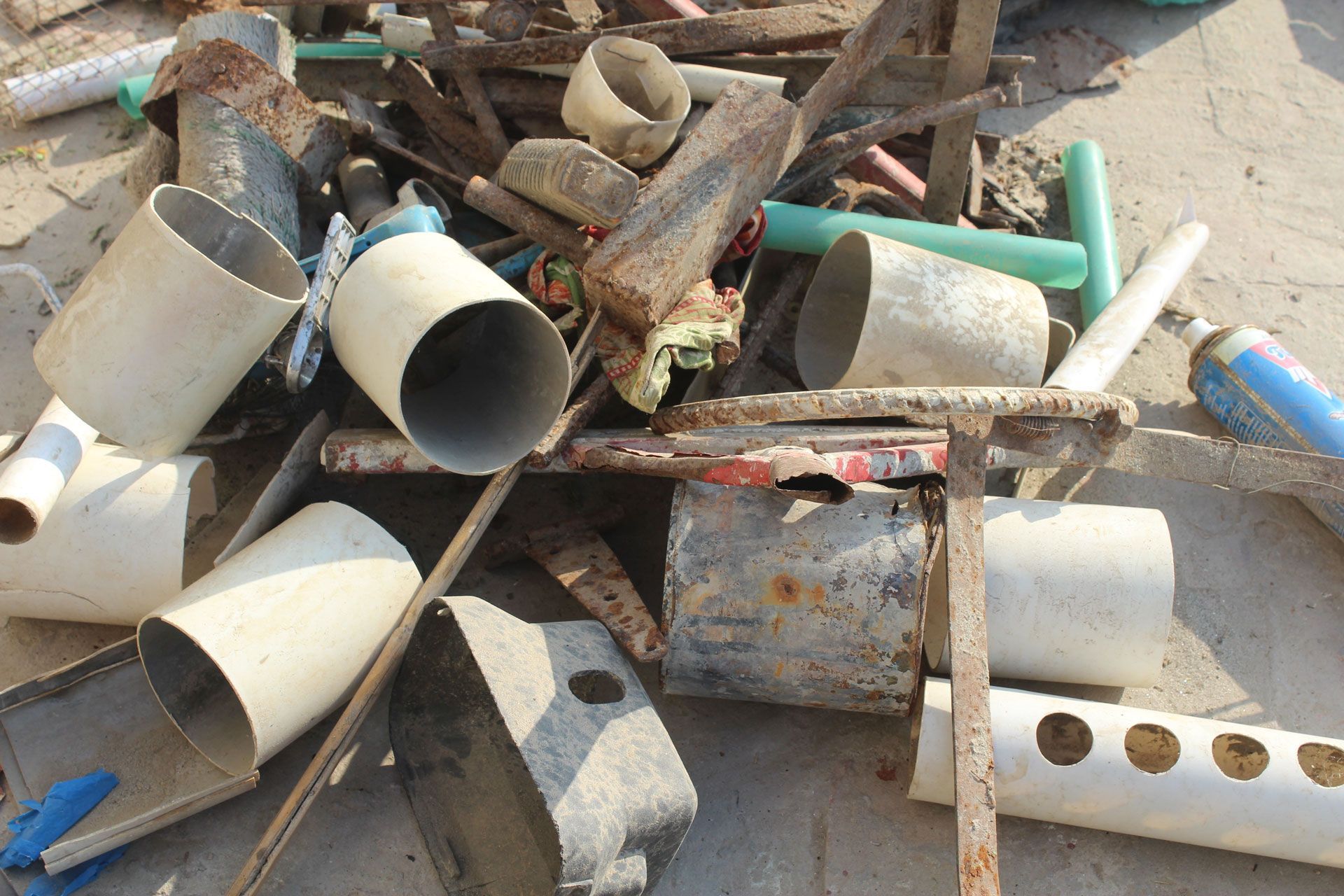 Pile of discarded metal and PVC pipes, wood scraps, and concrete debris on the ground.