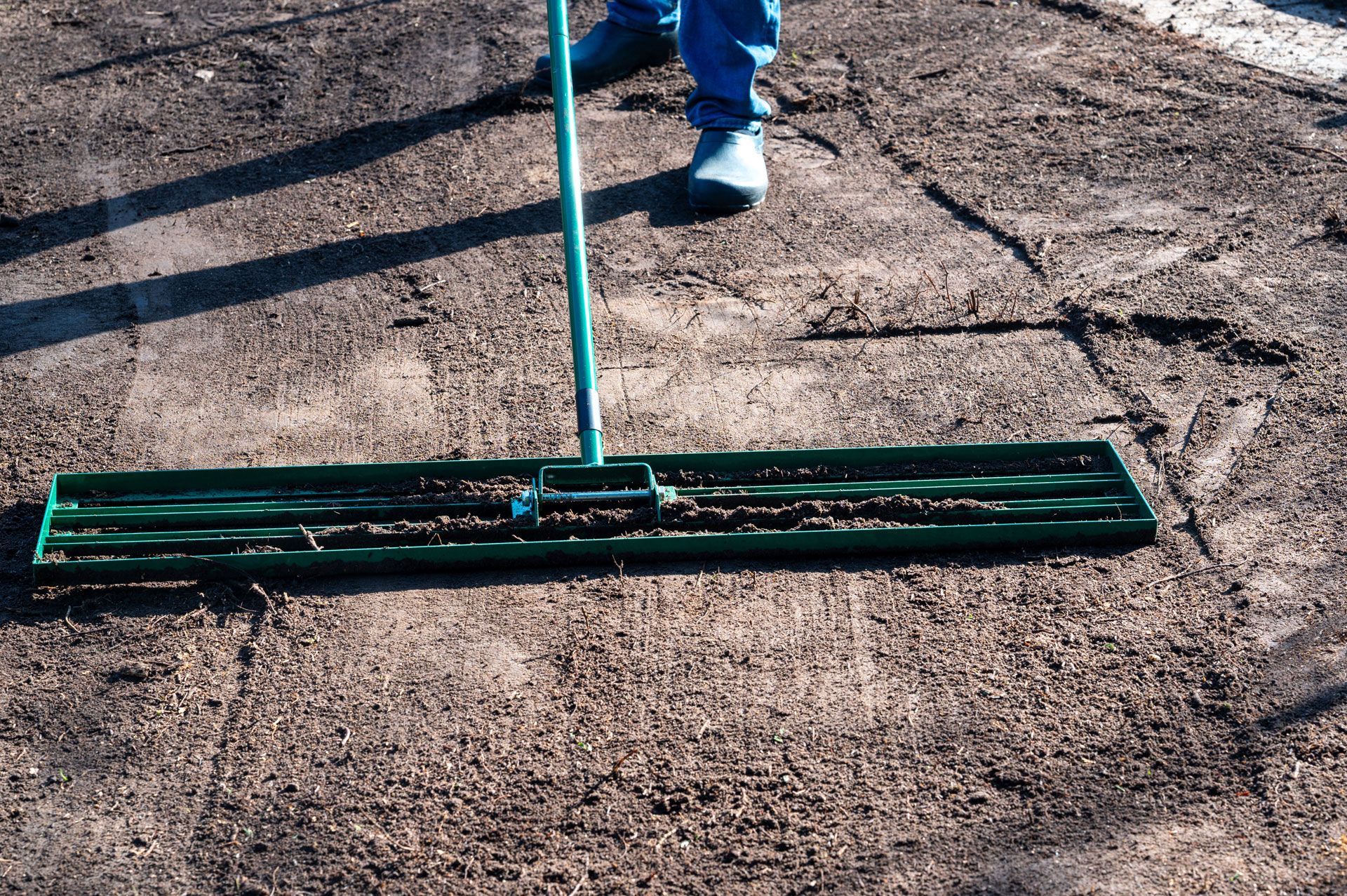 Person using a wide push broom to sweep dirt from a cracked outdoor surface