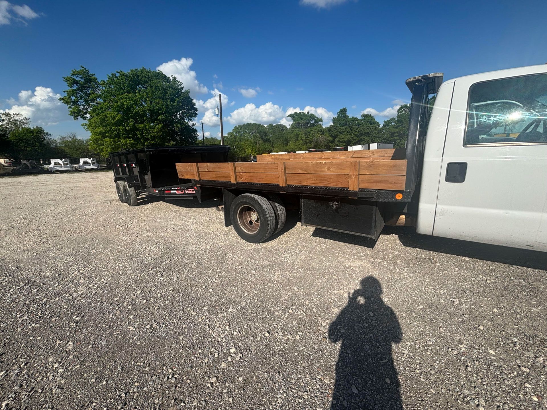 White flatbed truck loaded with lumber in a gravel lot under a bright blue sky