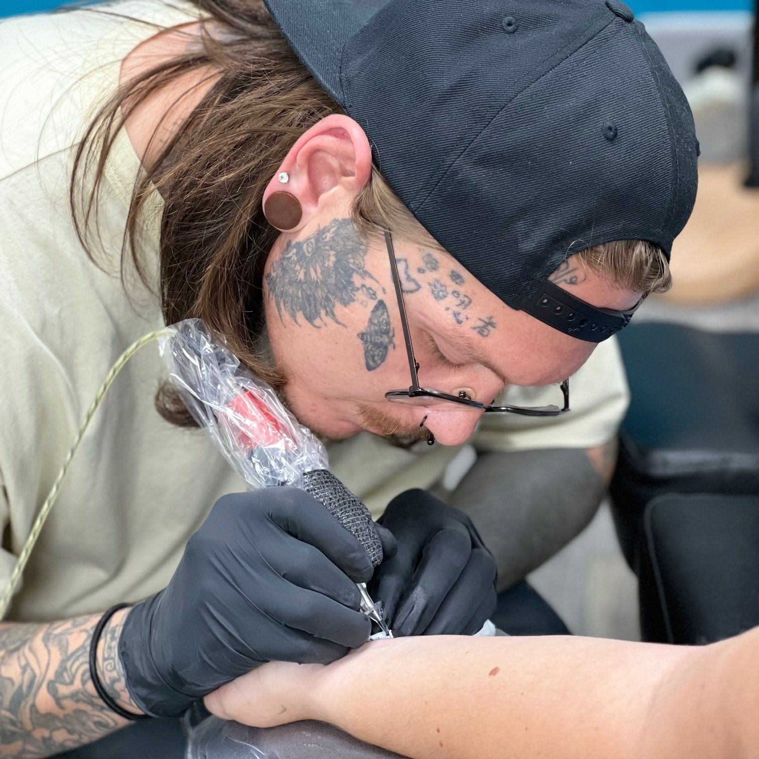 A man with tattoos on his face is getting a tattoo on another man 's arm.