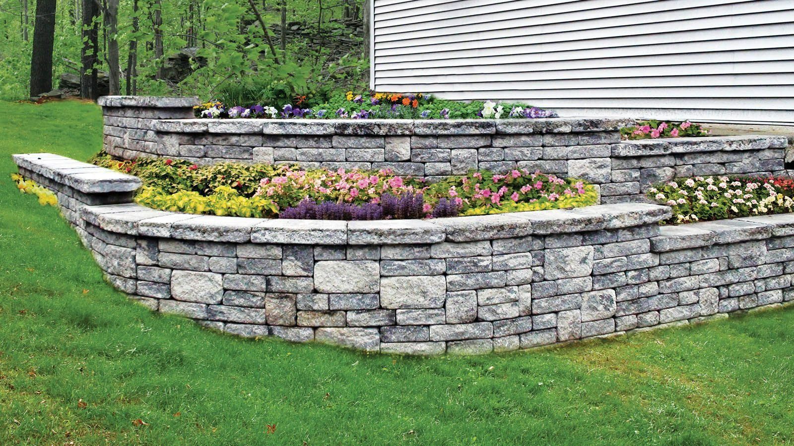 Stone retaining wall with colorful flowers in a residential yard.