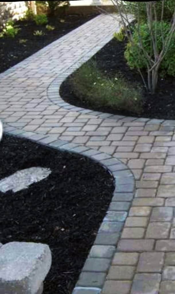 Brick pathway curving through dark mulch and garden beds.