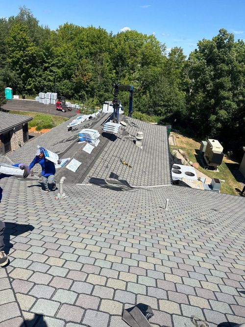 Worker installing roofing shingles on a steep roof under a cloudy sky