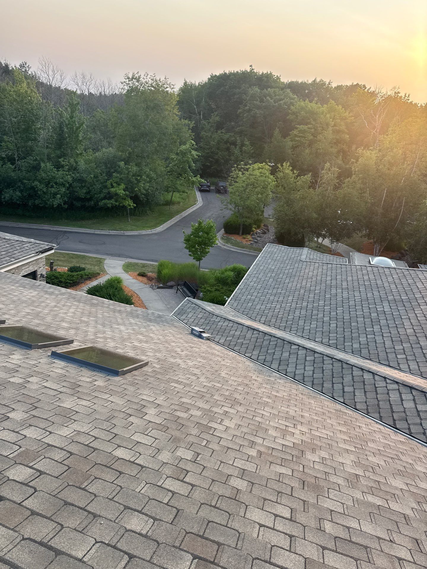 Worker installing roofing shingles on a steep roof under a cloudy sky