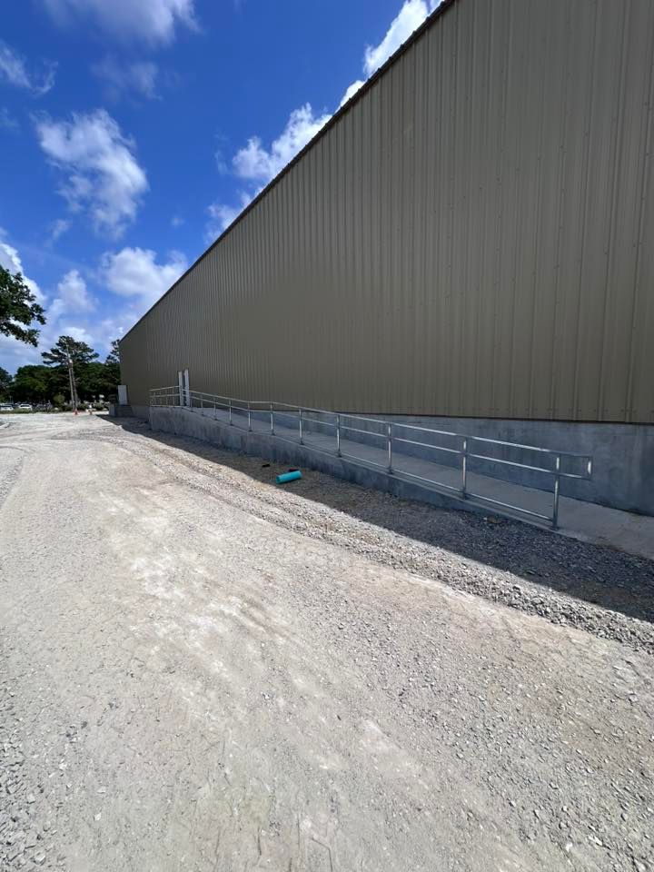 Gravel path alongside a building with metal siding and a low concrete wall with a metal railing.