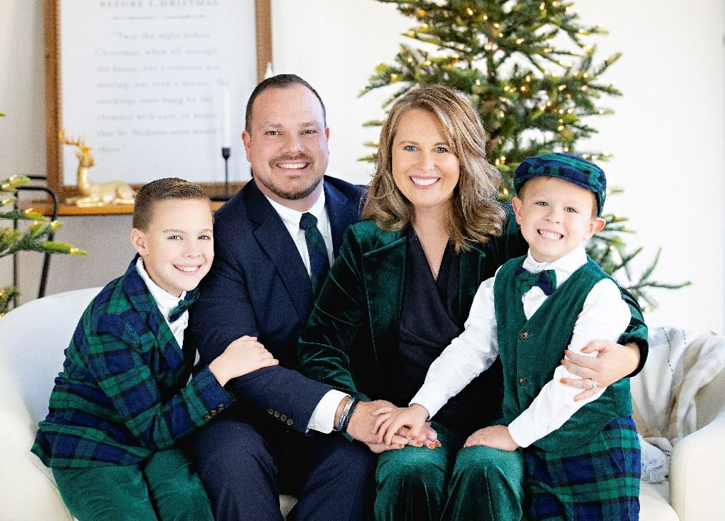 Family of four in formalwear smiles in front of a Christmas tree.