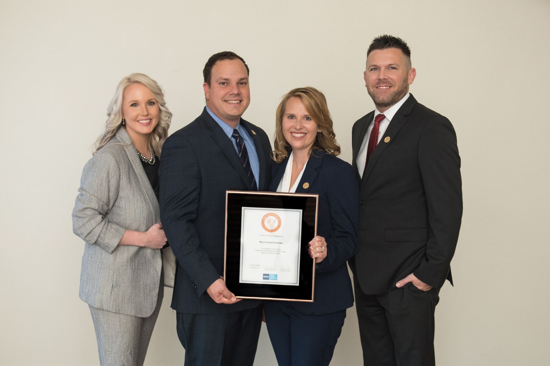 Four people in suits holding a framed award, smiling in a well-lit space.