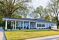 A light blue, single-story building with a covered entrance, a well-manicured lawn, and a sign.