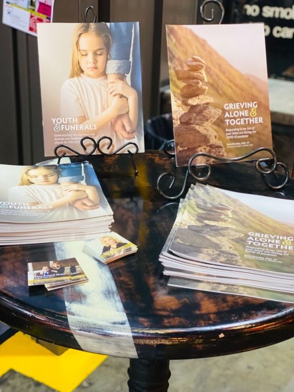 Informational table with brochures about youth and grieving. A young person in the first, rocks stacked, and a mountain in the other.
