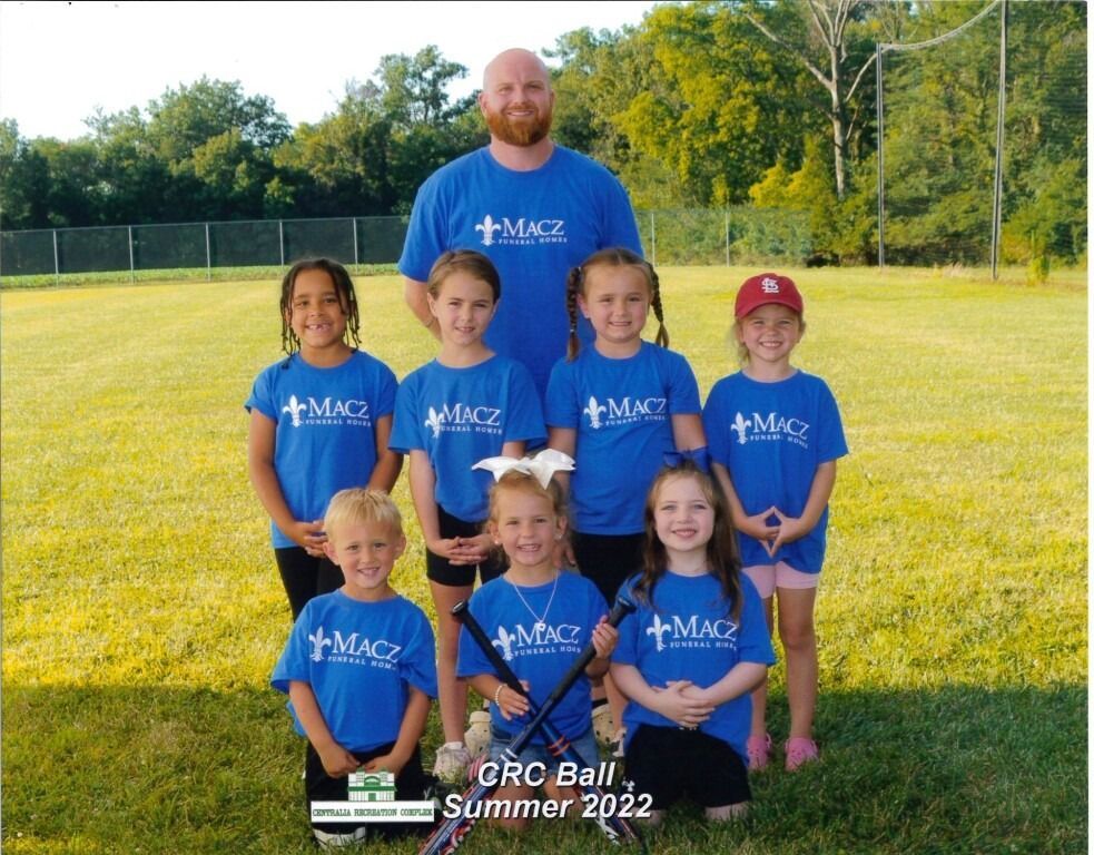 Youth baseball team in blue shirts with a coach, posing on a field.