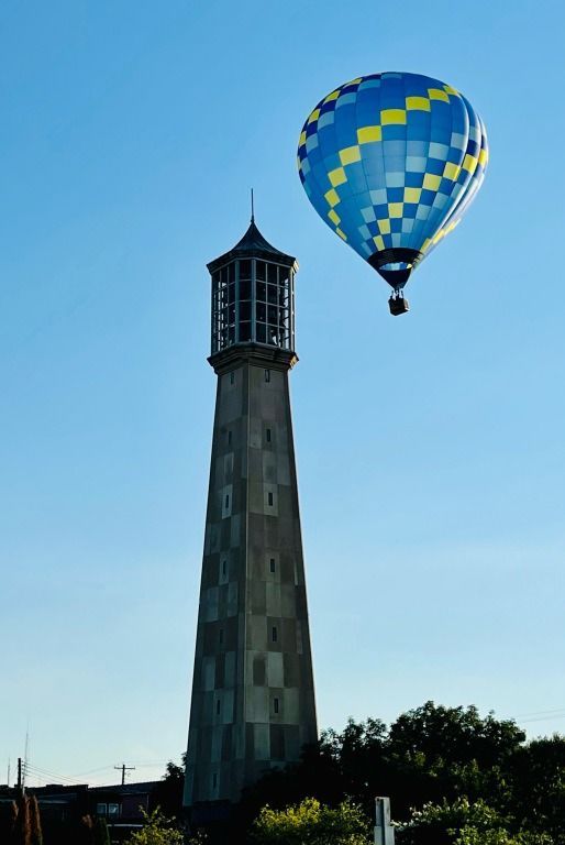 Tall stone lighthouse with a blue and yellow hot air balloon against a clear blue sky.