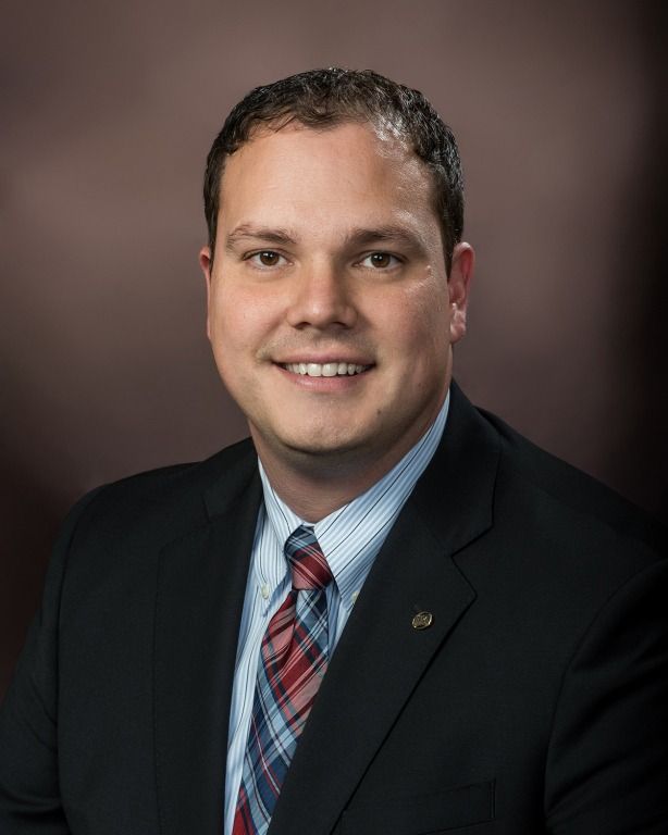 Man in suit smiles at the camera, against a dark, blurred background.