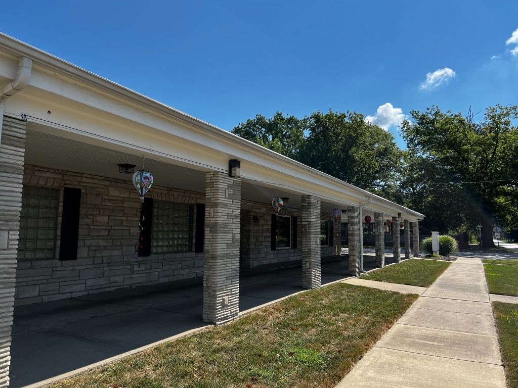 Exterior view of a long, single-story building with stone pillars and a walkway on a sunny day.