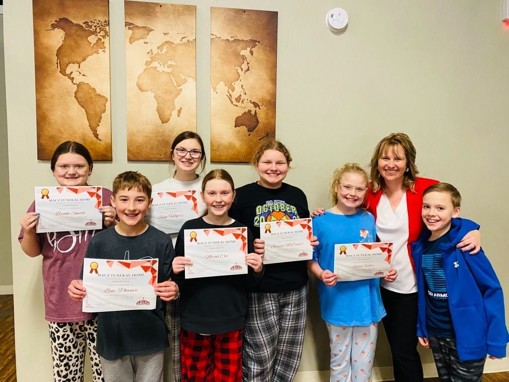 Group of children and a woman holding certificates in front of world map decor.