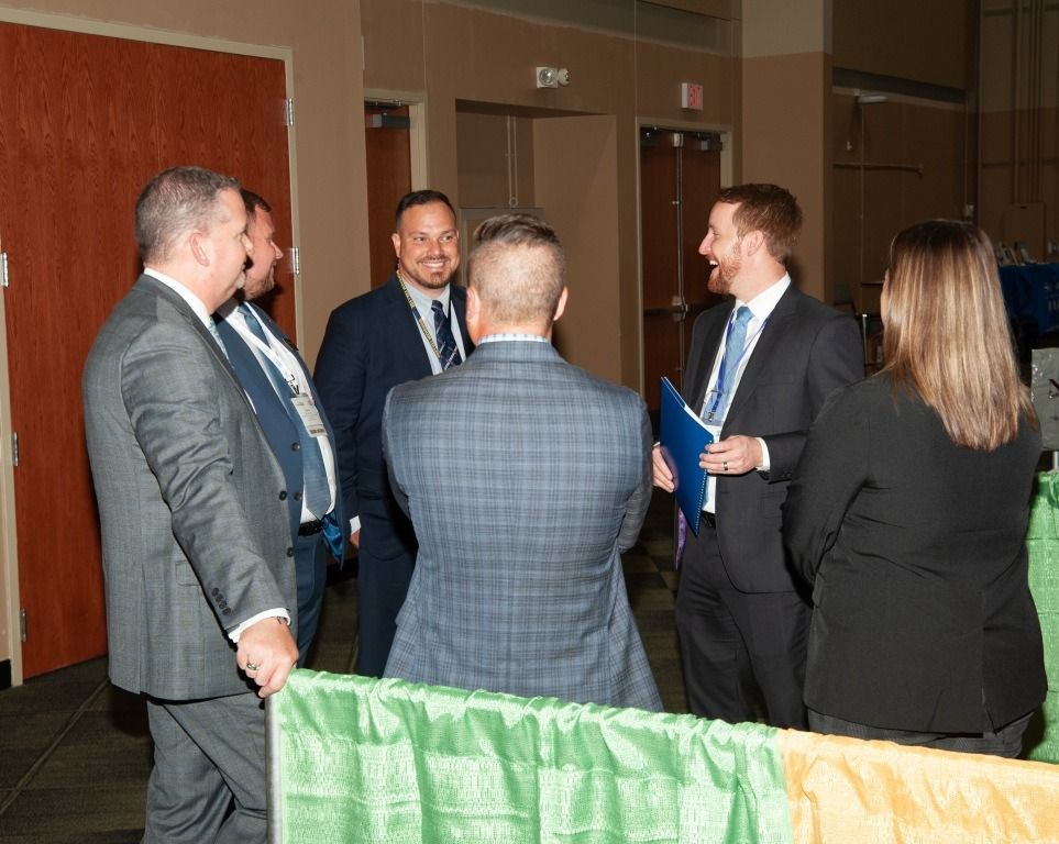Group of people in suits talking at an event; some holding papers.
