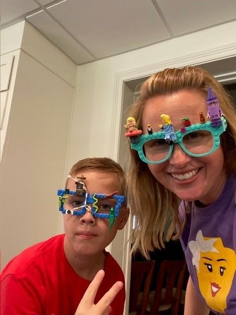 Person and child wearing glasses decorated with Lego bricks, smiling.