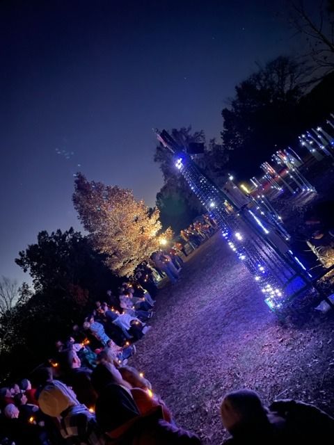 People gathered outdoors at night, illuminated by blue and white lights, possibly for a holiday event.