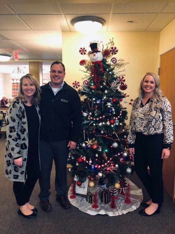 Three people pose by a decorated Christmas tree in an office setting.