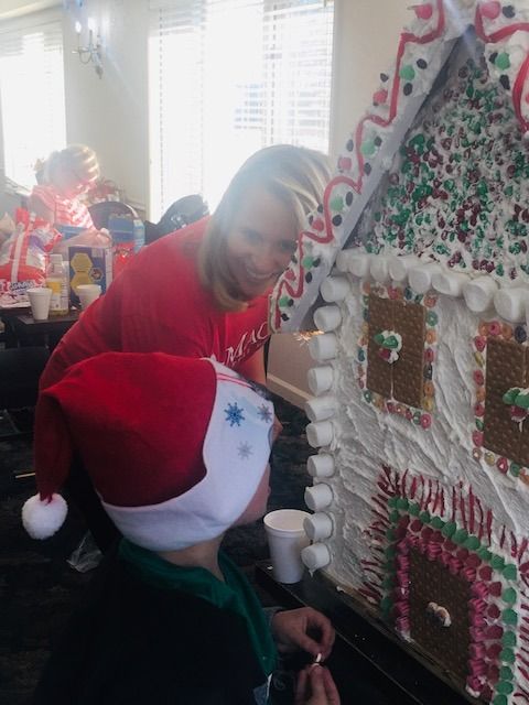 Woman and child decorating a large gingerbread house with candy and frosting.