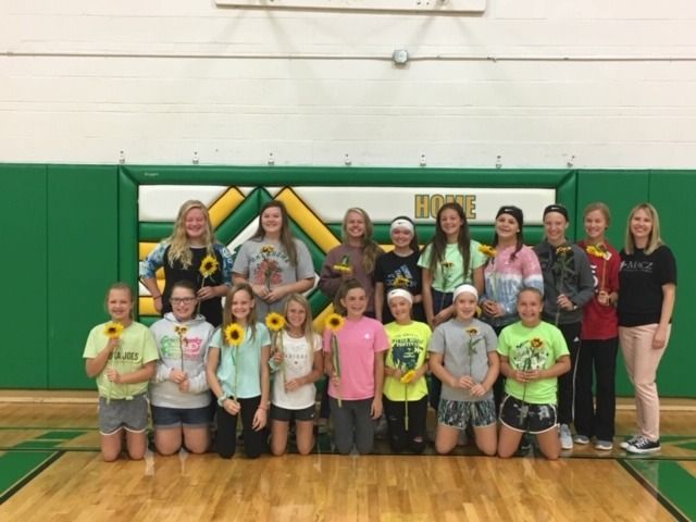 Group of people holding sunflowers in a gymnasium. Green and yellow wall with 