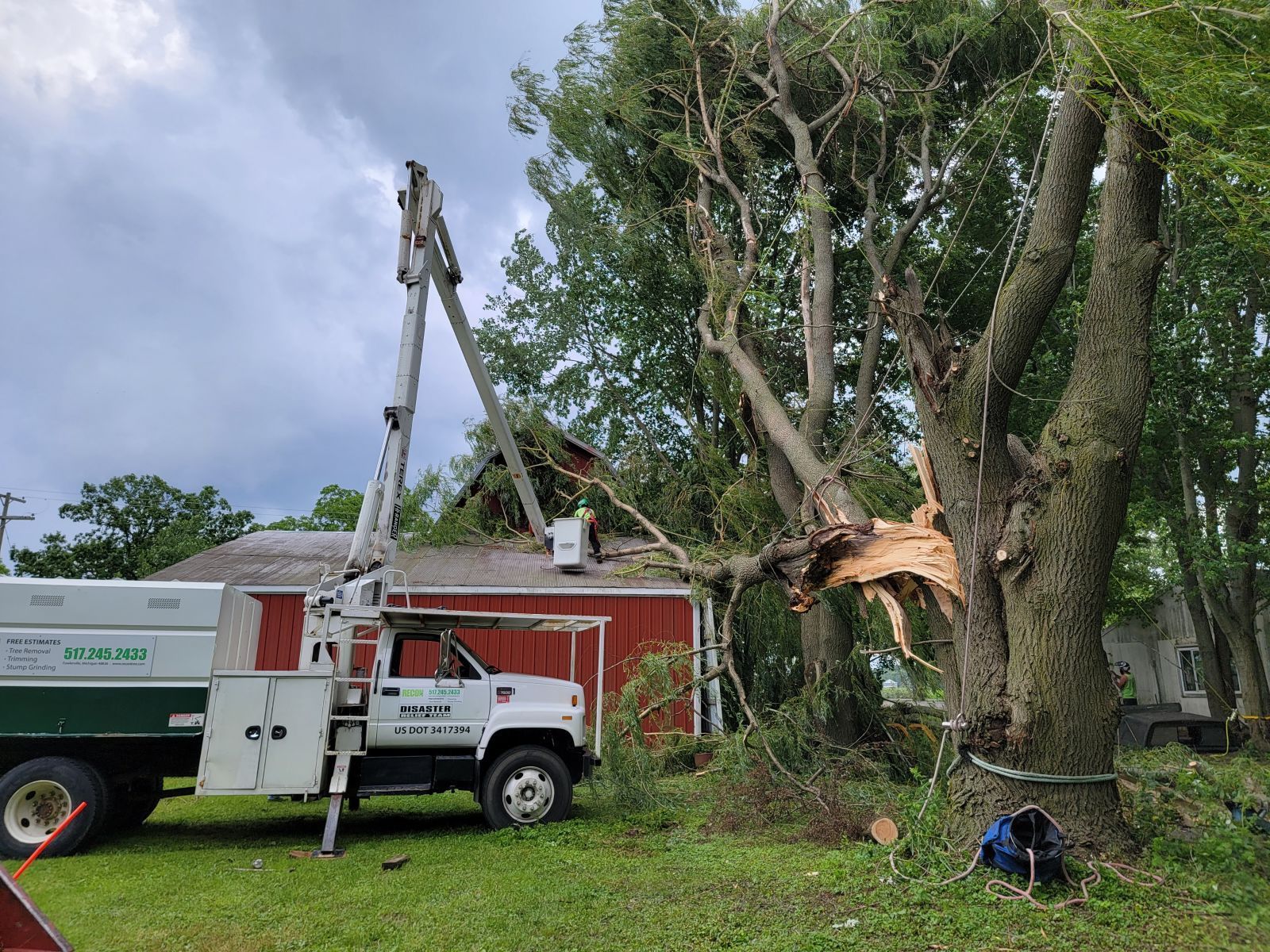 A white truck is parked in front of a house with a tree fallen on it.