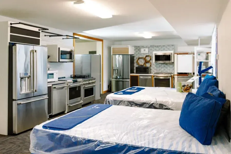 A bedroom with two beds and a kitchen with stainless steel appliances.