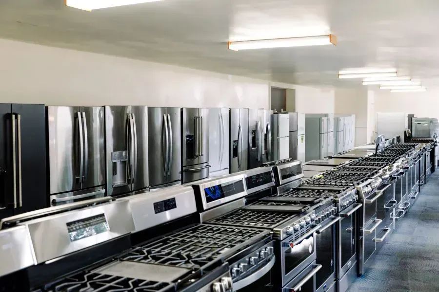 A row of stove tops and refrigerators in a kitchen showroom.