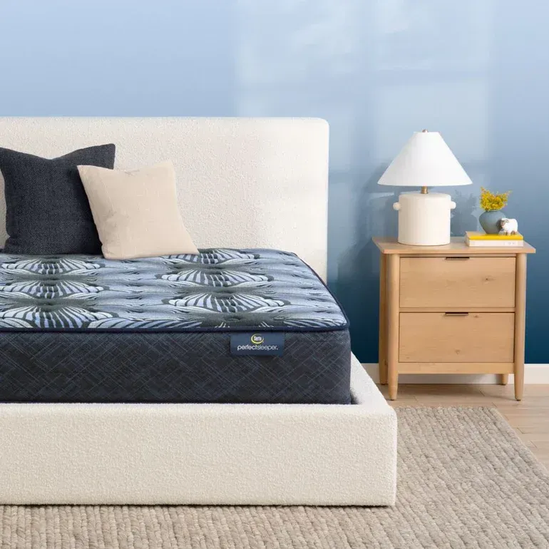 A bed with a mattress and pillows next to a nightstand