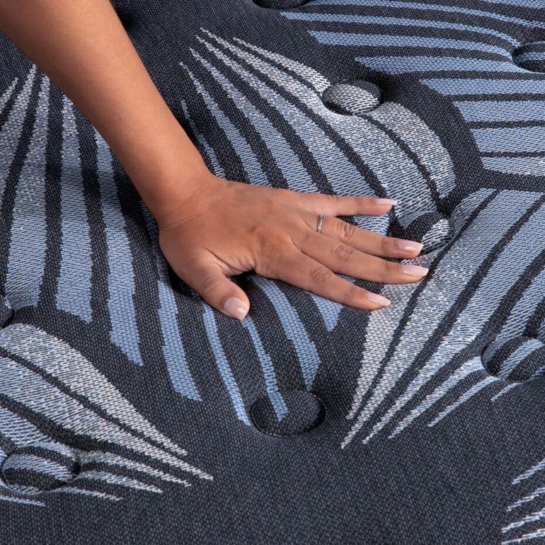 Hand pressing on a gray patterned upholstered cushion with button tufts