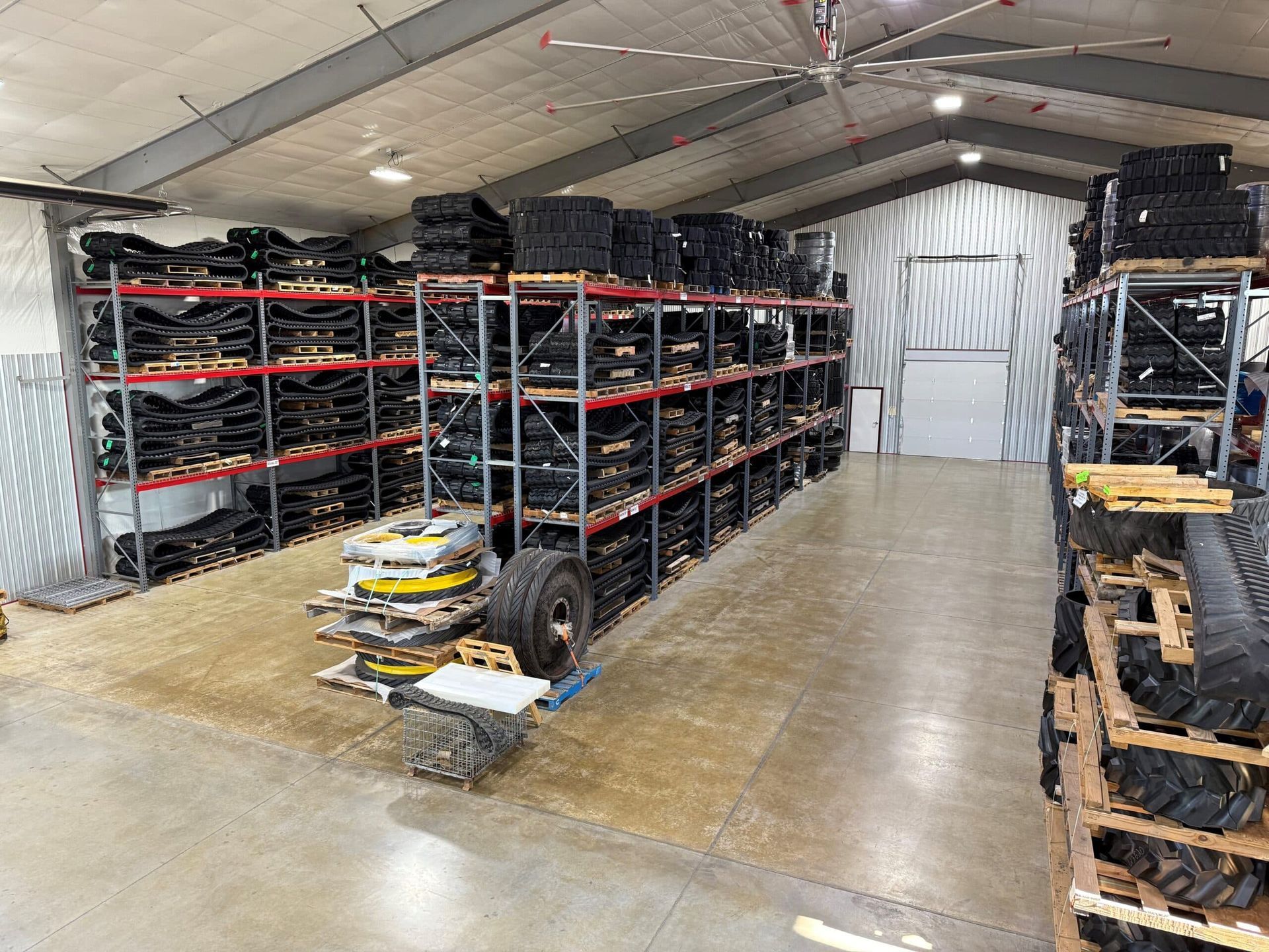 Warehouse with metal shelving stacked with tires and auto parts, showing a wide concrete aisle and closed back door