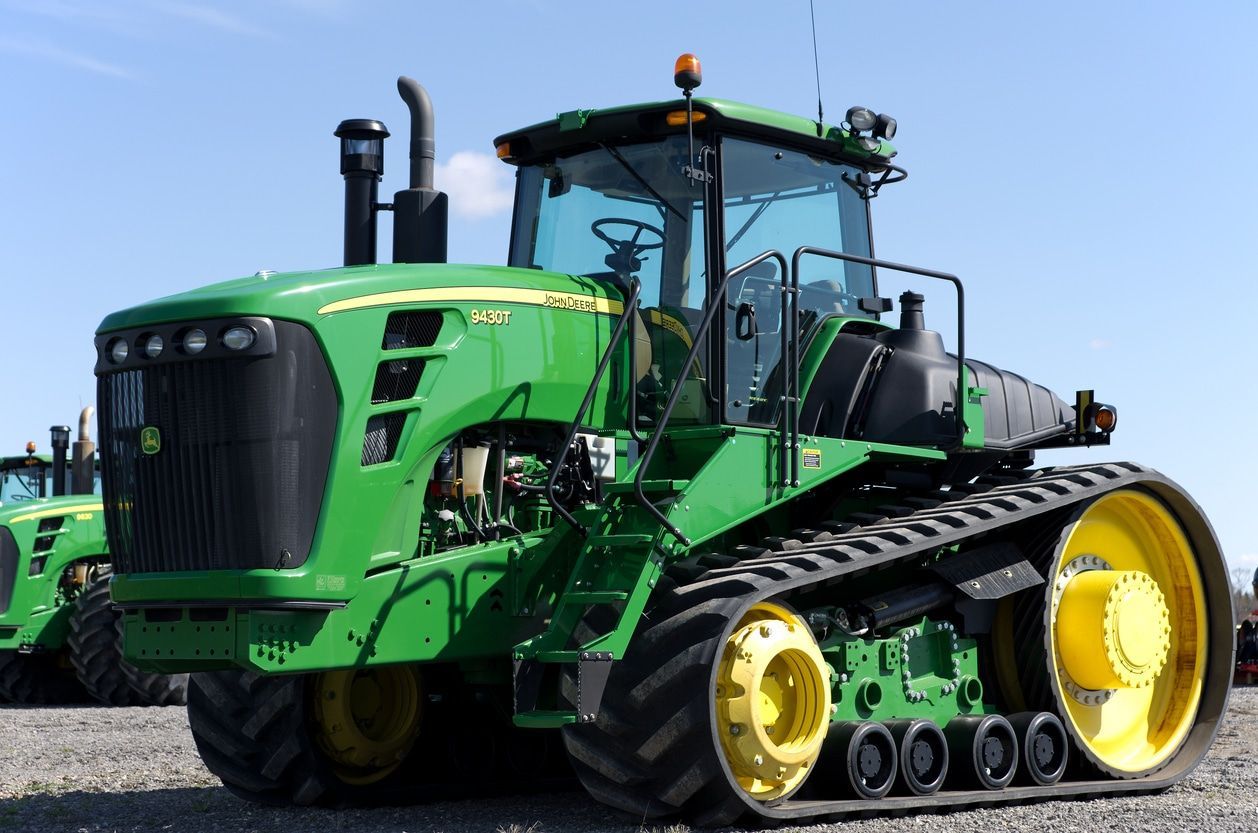 Green agricultural tractor with large yellow wheels on a gravel road, side view