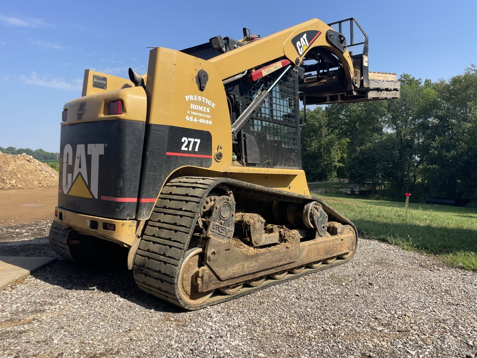 CAT tracked loader on gravel, with raised bucket arm against a blue sky