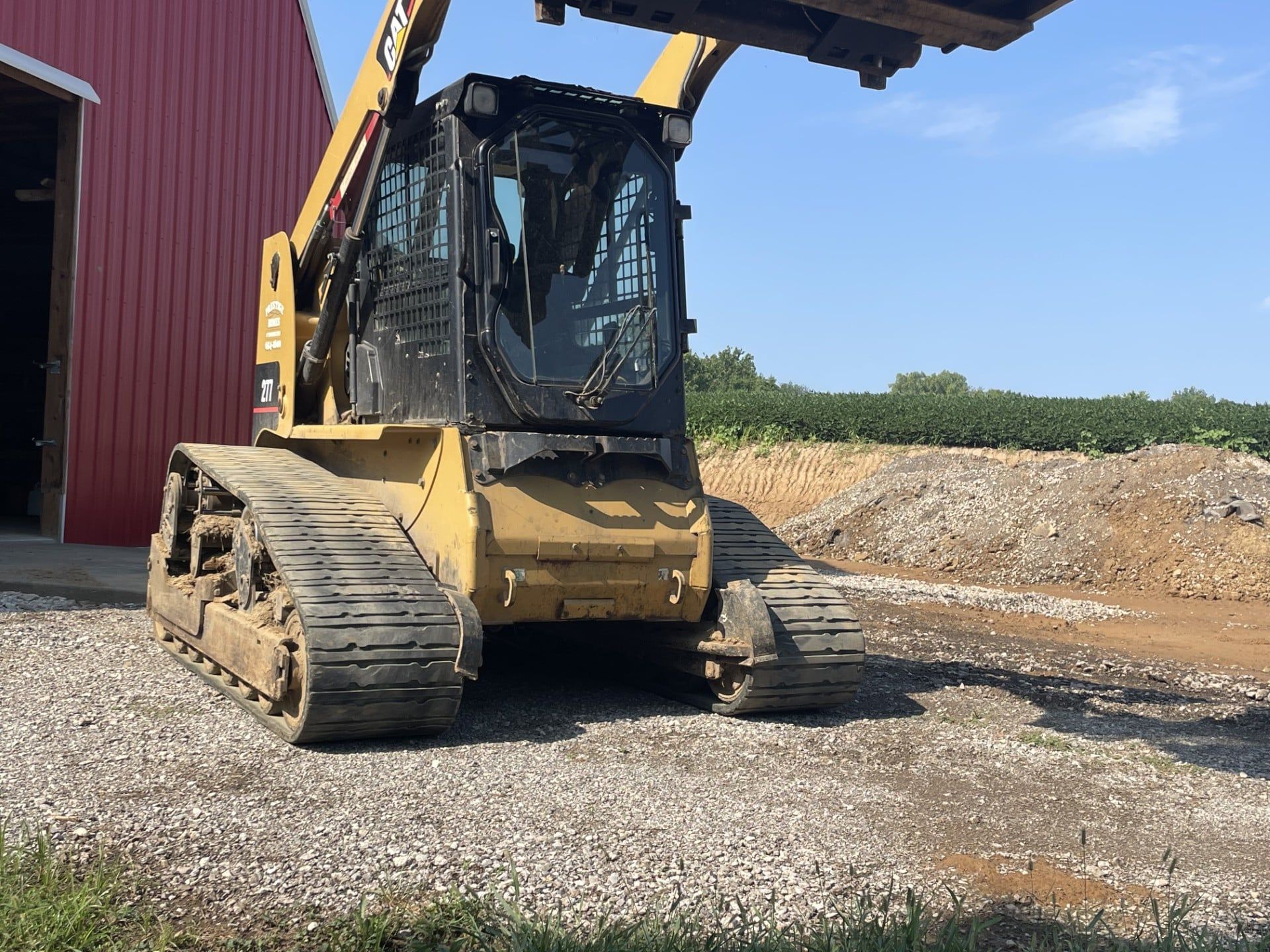 Yellow tracked construction loader on gravel beside a red building under a blue sky