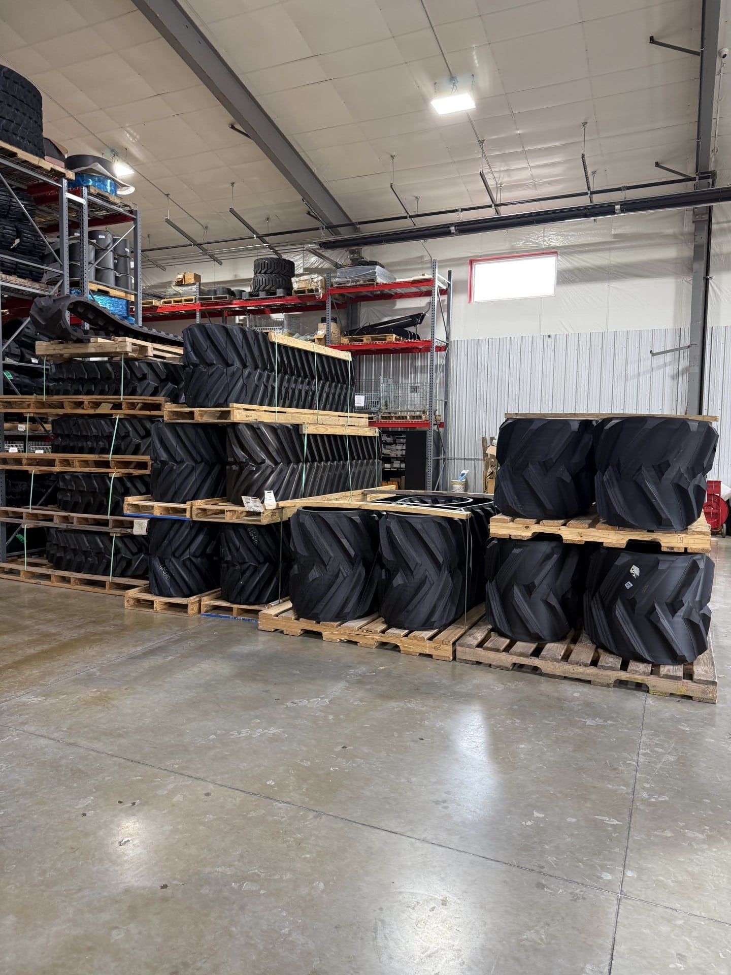 Warehouse aisle with stacked pallets of large black-wrapped rolls and metal shelving.