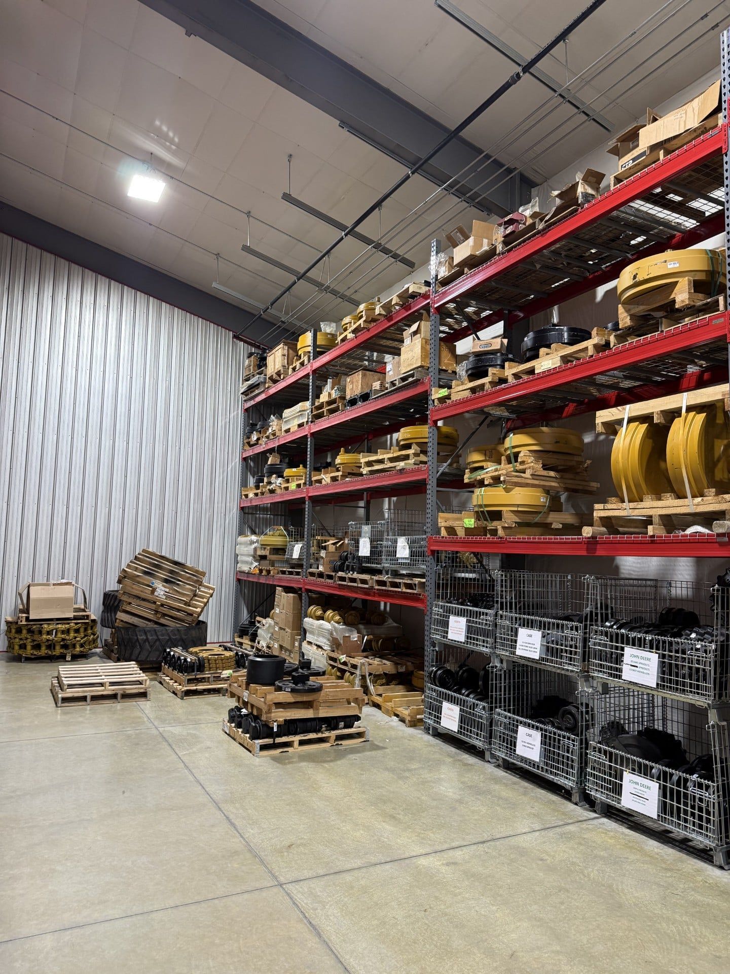 Warehouse aisle with tall red shelving, stacked pallets, and industrial parts on the floor