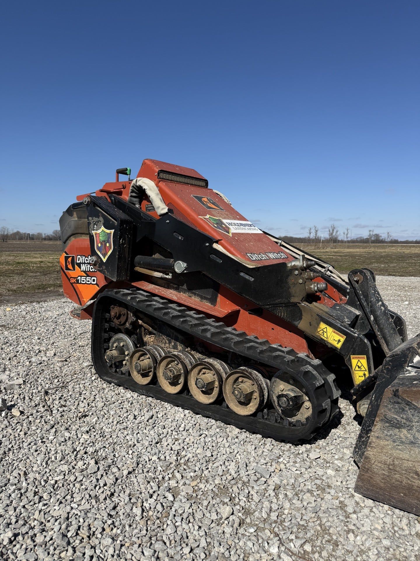 Orange tracked skid steer with bucket on gravel under a clear blue sky