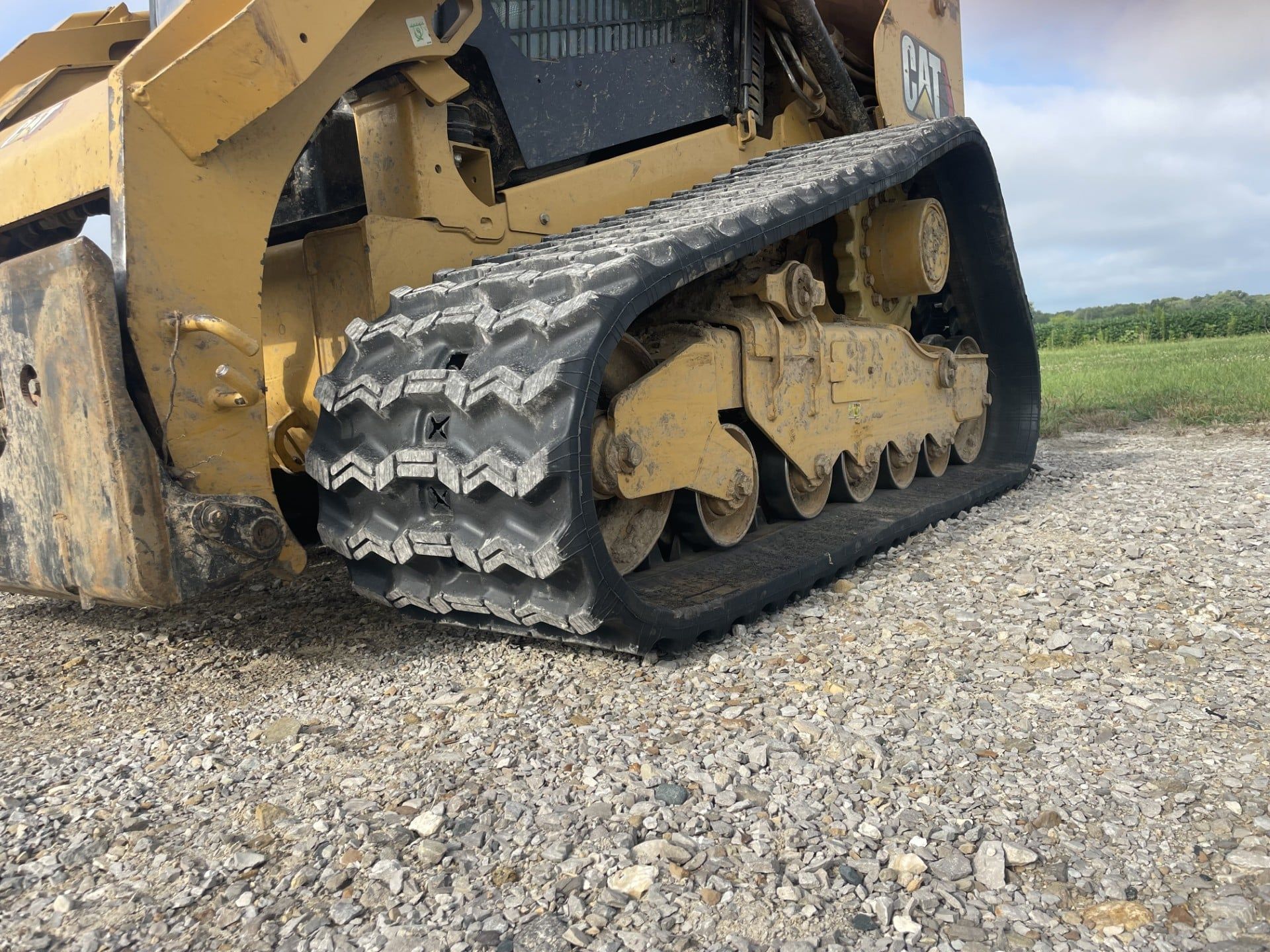 Yellow tracked construction machine on gravel, shown close-up with its rubber track and blade assembly.