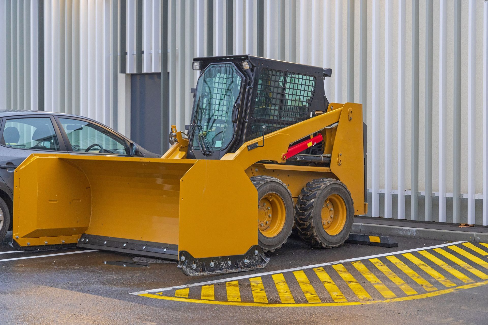 Yellow front loader parked beside a striped curb outside a corrugated metal building.