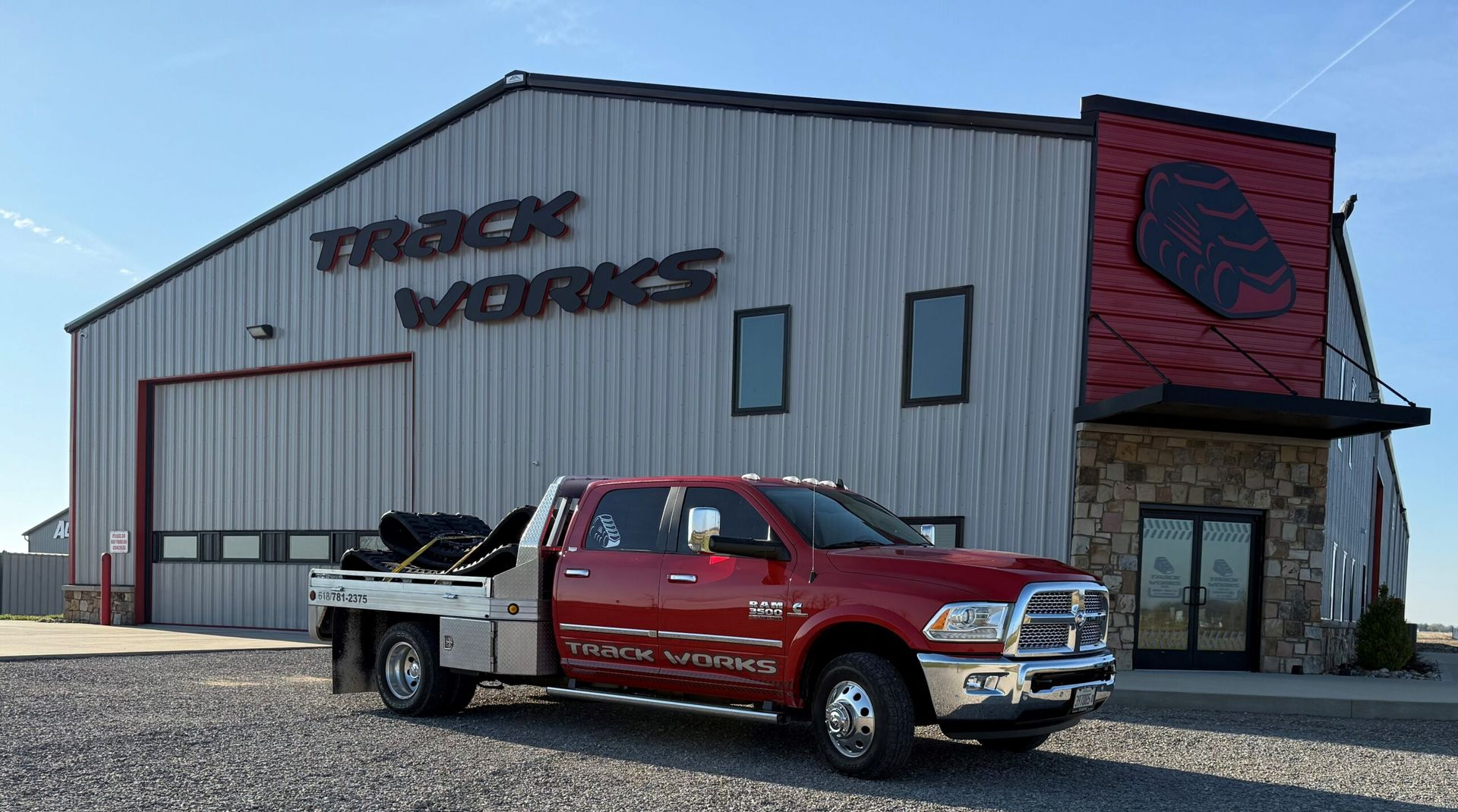 Red tow truck parked outside a gray-and-red work garage with large black lettering.