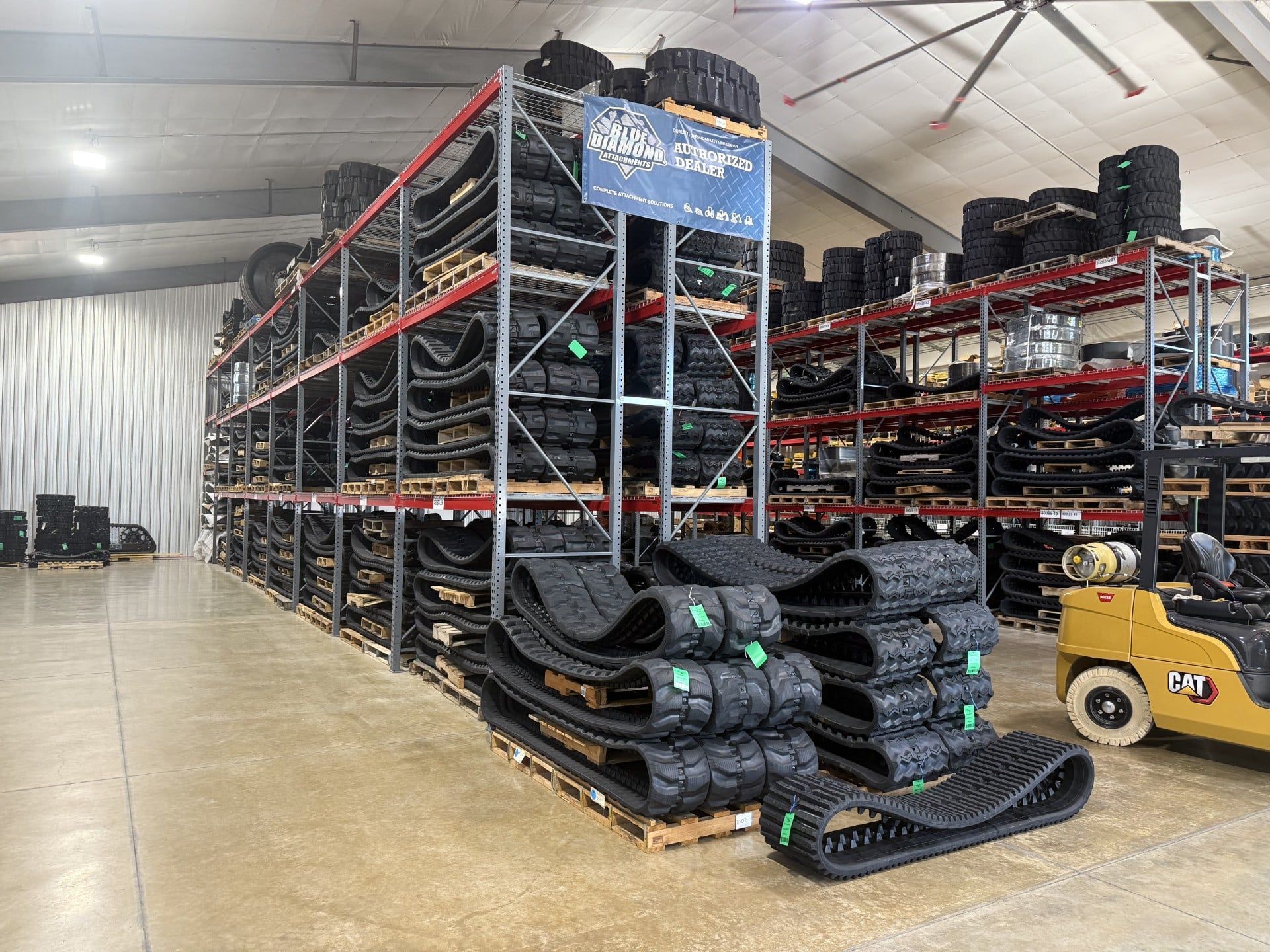 Warehouse aisle with stacked black tires on metal racks and a yellow forklift under a tented roof.