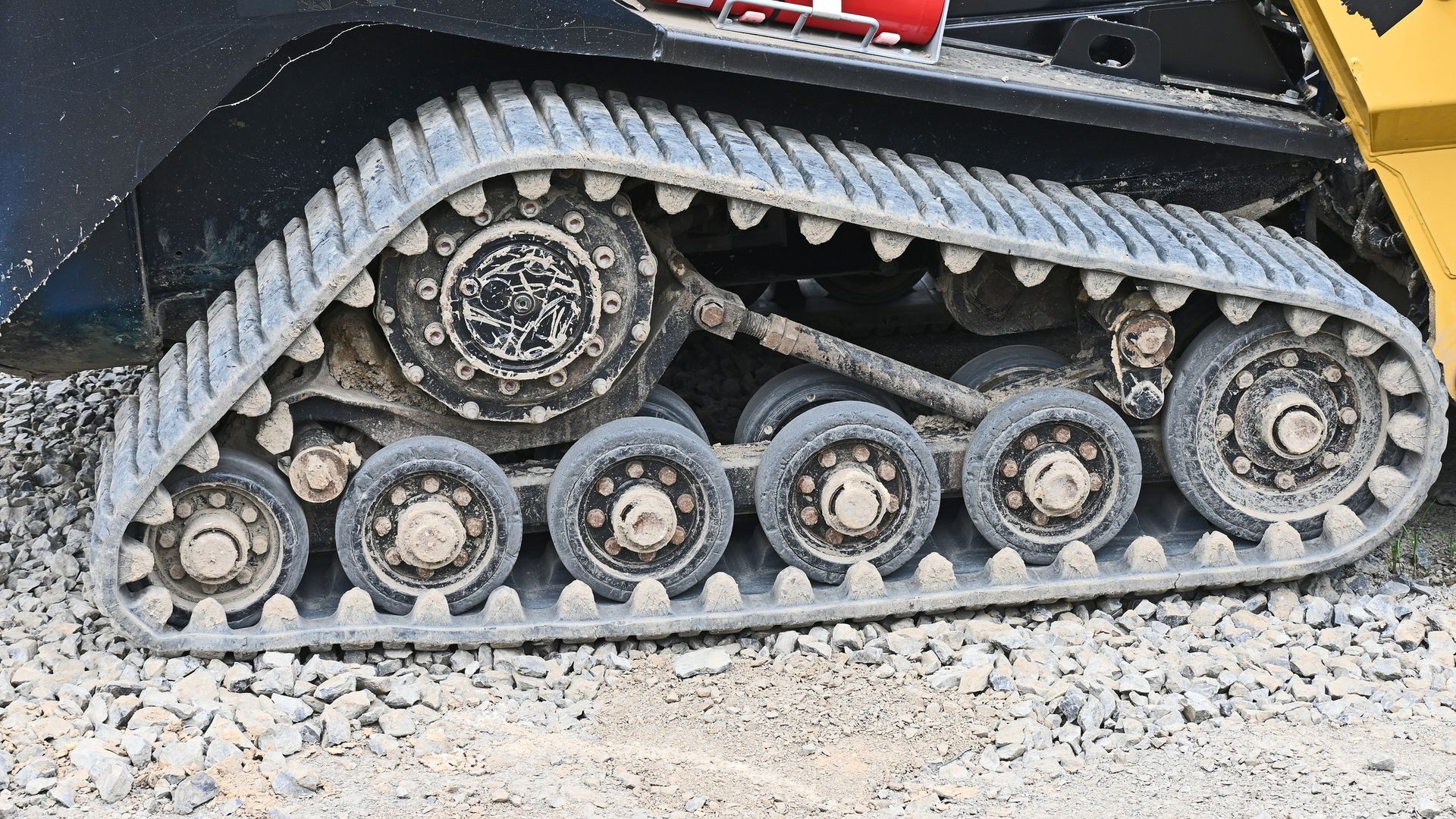 Close-up of a tracked vehicle’s undercarriage with road wheels and rubber treads on gravel.