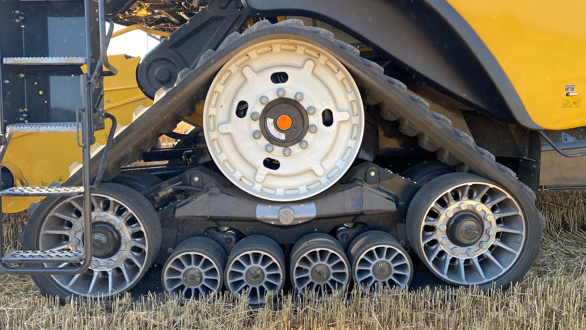 Close-up of a yellow tracked machine’s wheel and rubber treads on grass