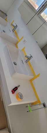 Bright bathroom with three white sinks, yellow handrails, and cleaning supplies on a counter