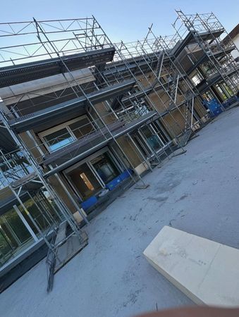 Tilted view of a building facade under construction with metal scaffolding and a dusty ground