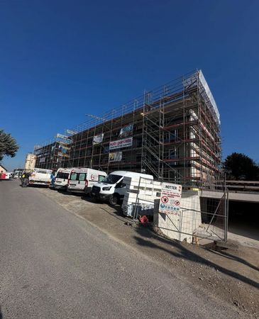 Scaffolding around a building under construction beside parked white vans on a sunny street