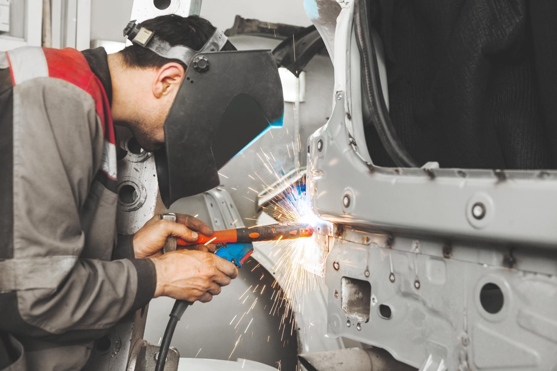 A person welding car bodywork, wearing a protective mask, generating sparks in a workshop.