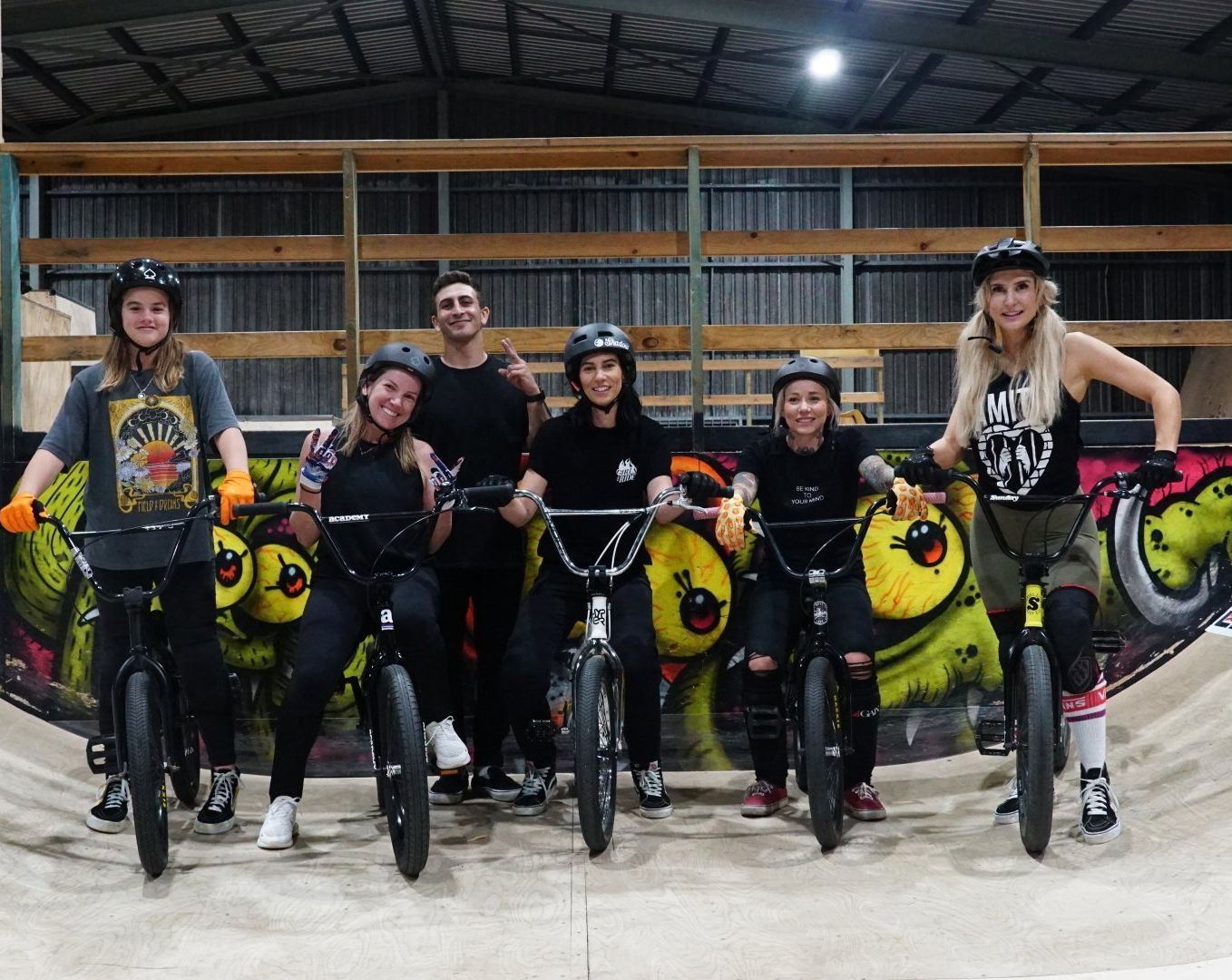 A group of people are posing for a picture while riding bicycles in a skate park.