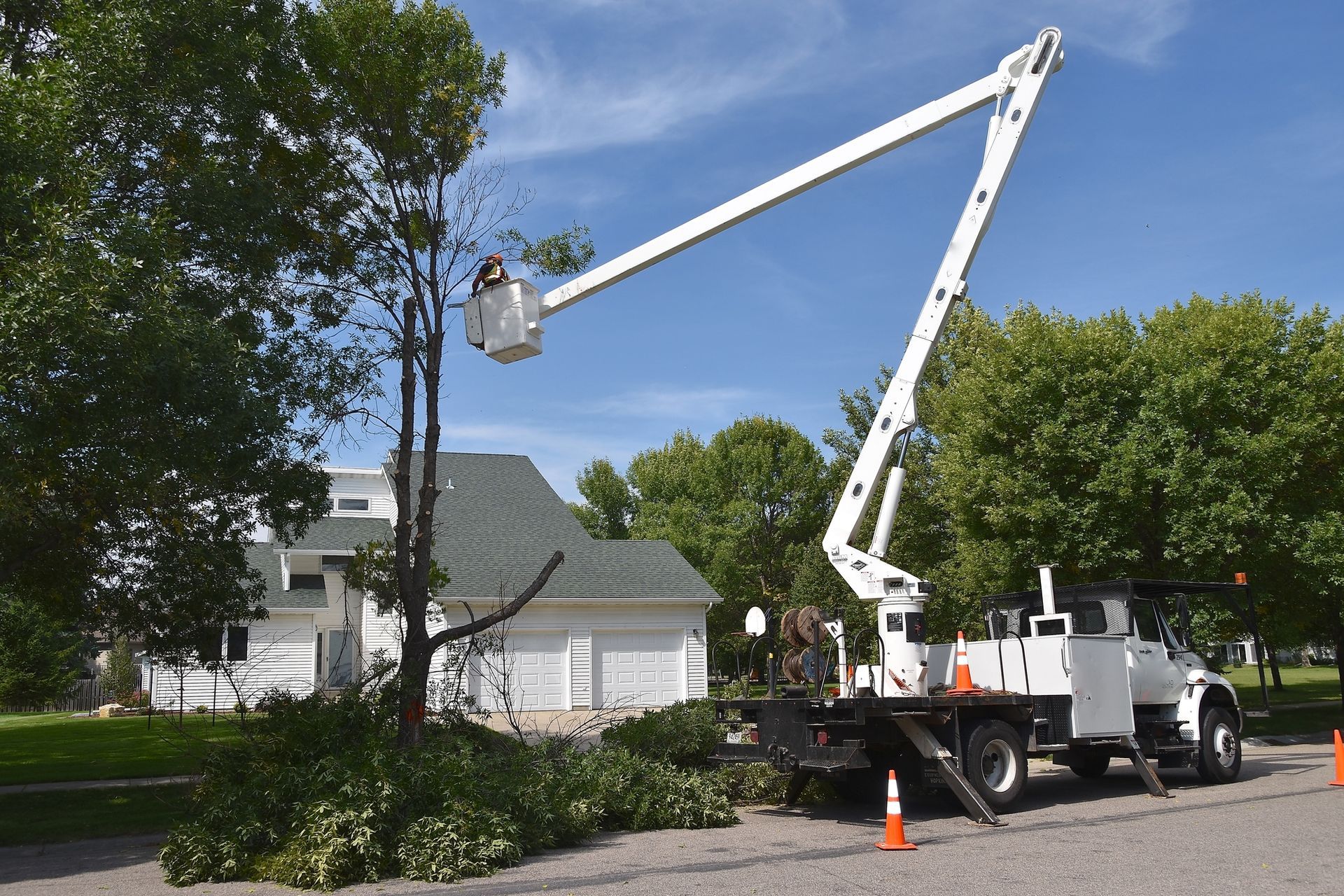 A crane is cutting a tree in front of a house