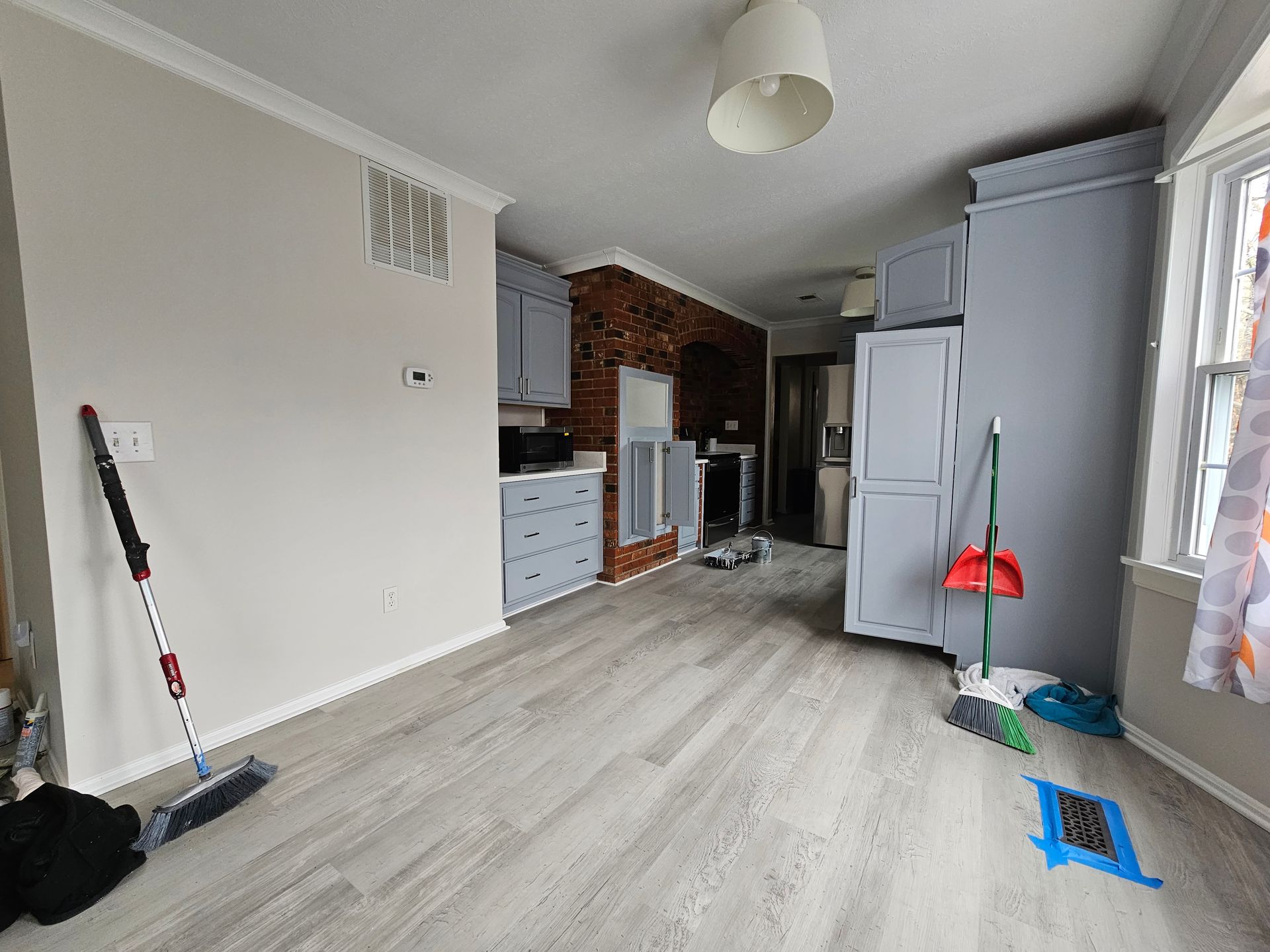 Empty living room being renovated, with cleaning tools, white cabinets, and a brick fireplace.