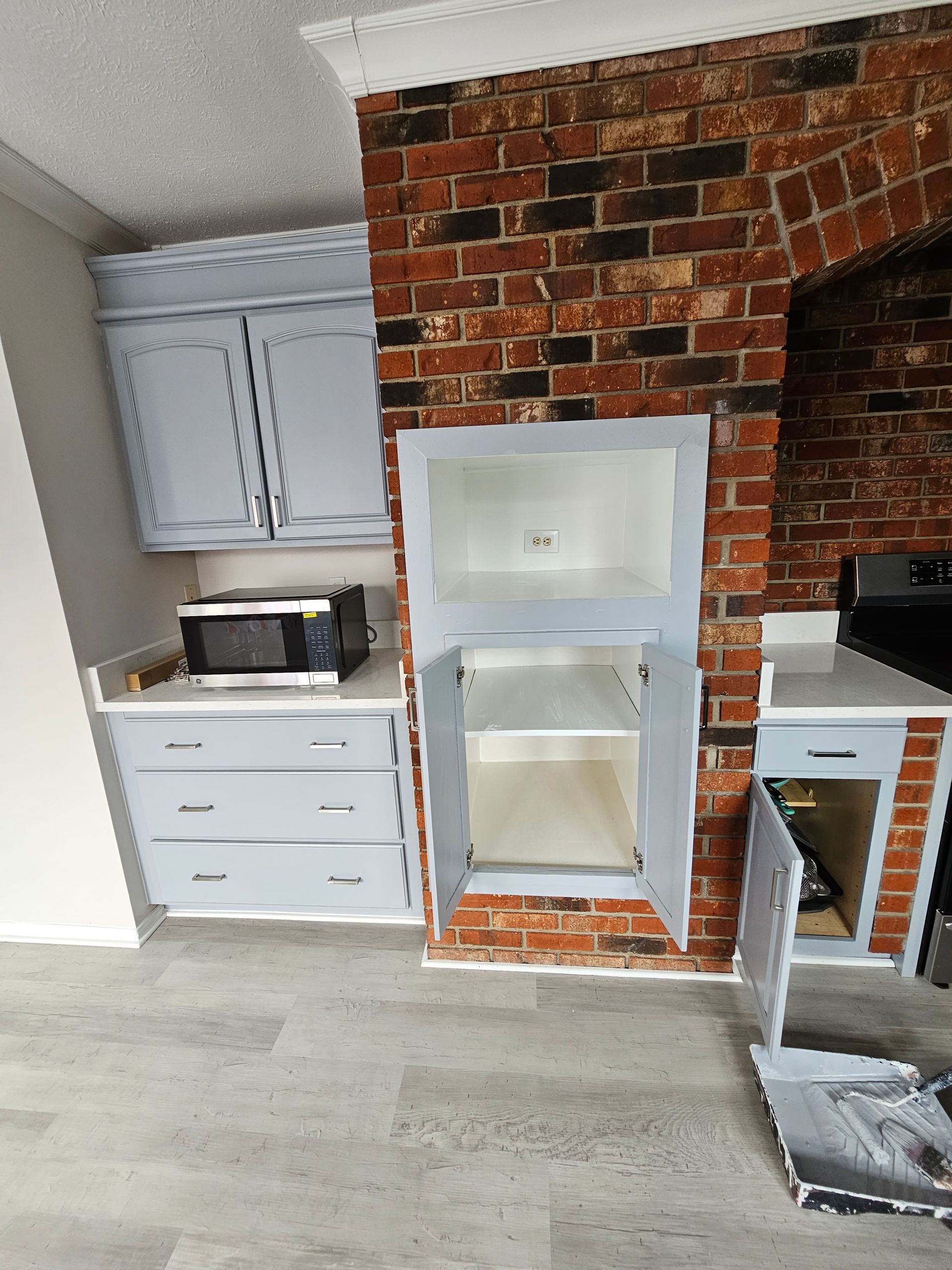 Kitchen alcove with white cabinets, a brick surround, and a built-in shelf opening.